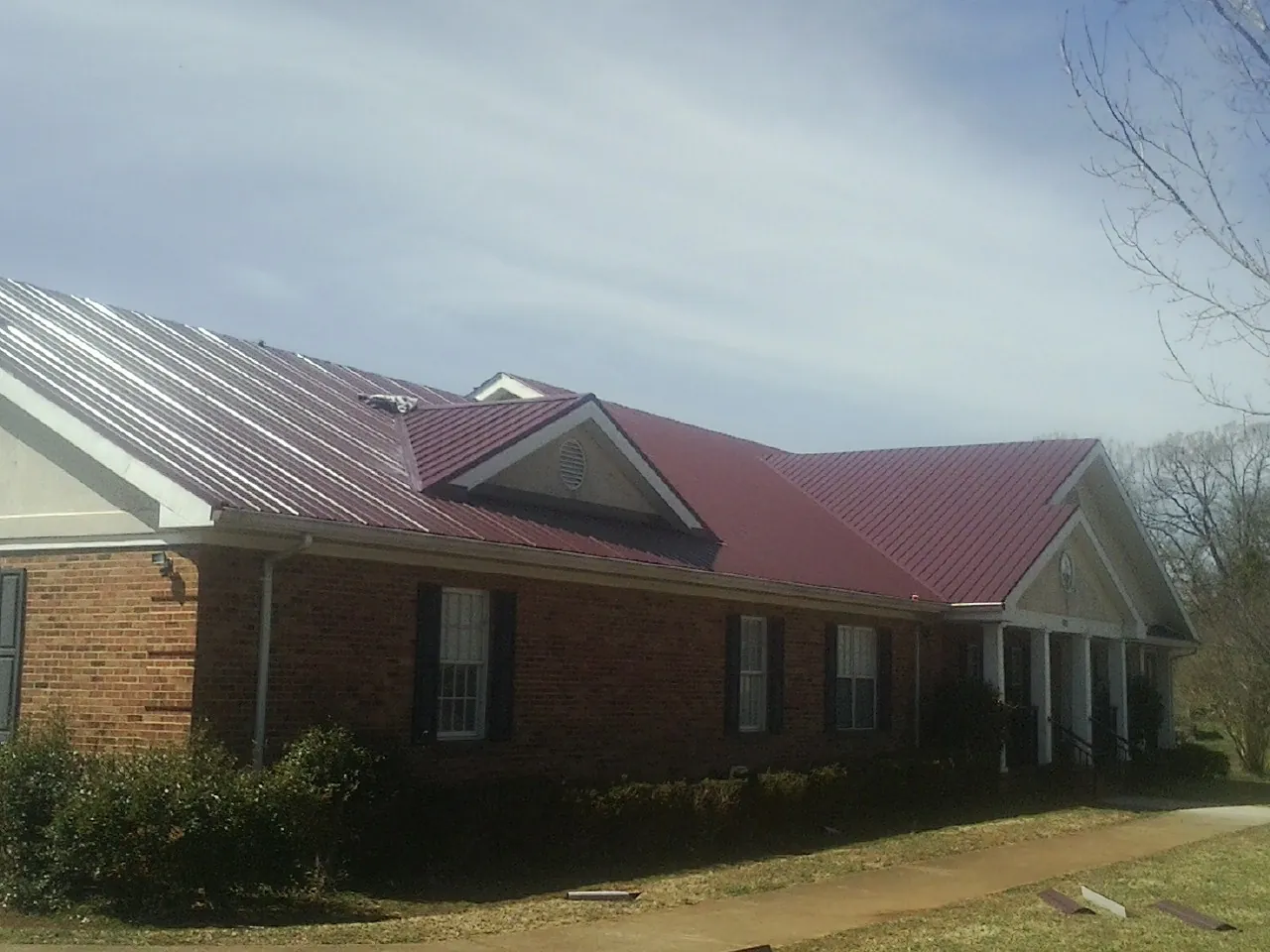 Red metal roof with gabled entries on a long brick building, from a Hail Damage Roof Repair job in Leetonia