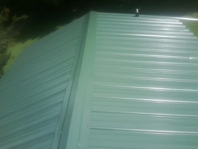 New green metal panels meeting at the ridge of a roof — Flat Roof Repair work by our crew in Leetonia