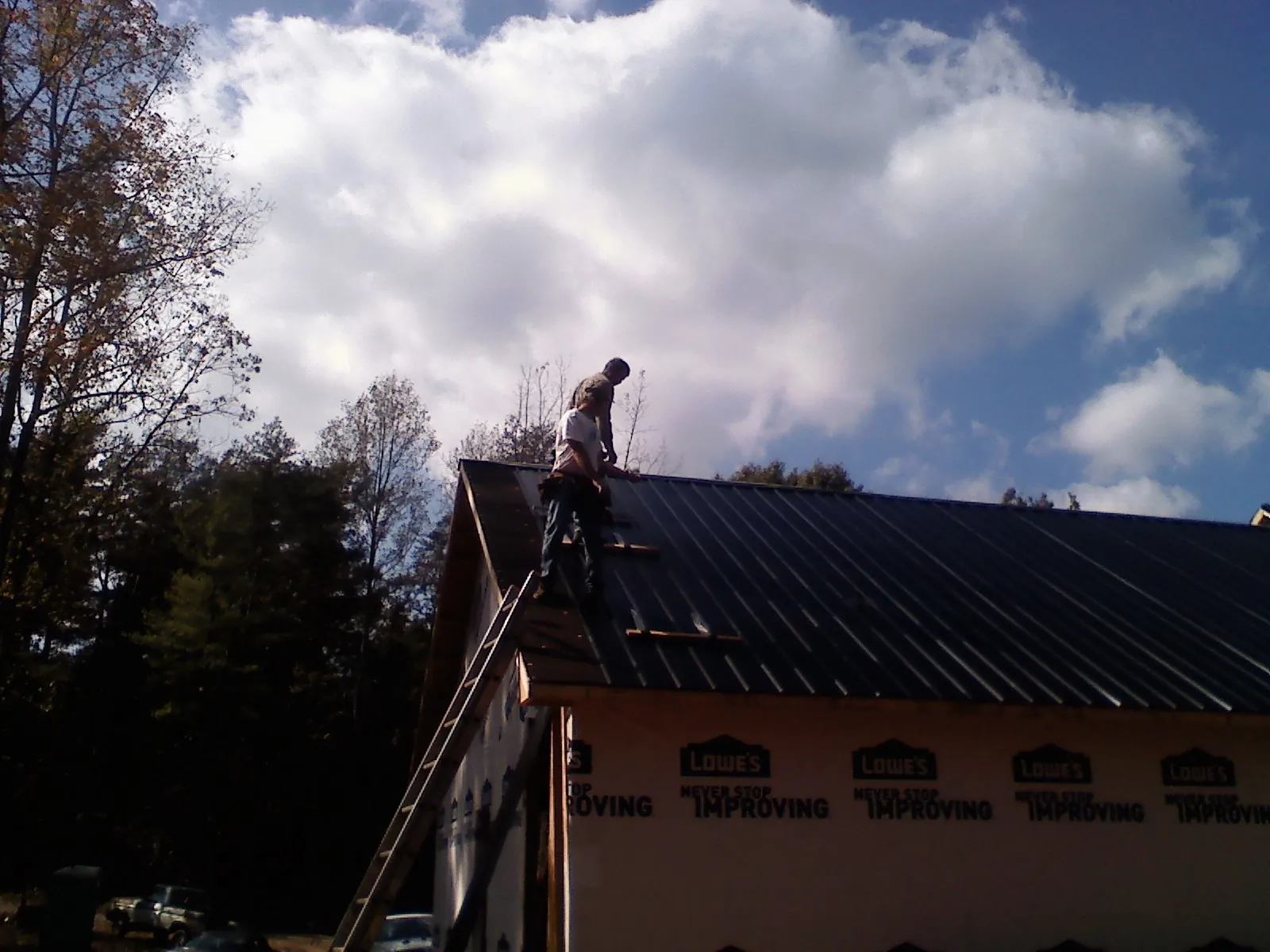 Roofer fastening dark metal panels high against a cloudy sky, from a Roof Inspection job in Leetonia