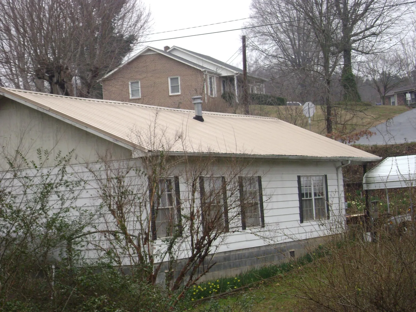 Tan metal roof on a white sided house set into a hillside — Commercial Roofing by Roofing Brothers in Leetonia