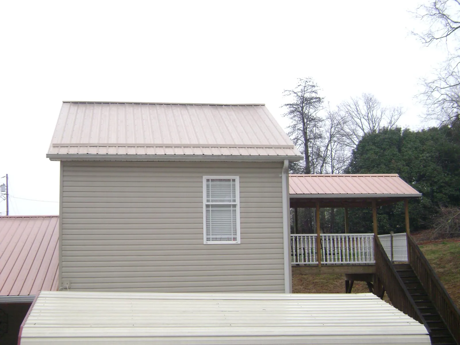 Tan metal roofs on a two story addition and attached porch, from a Roof Replacement job in Leetonia